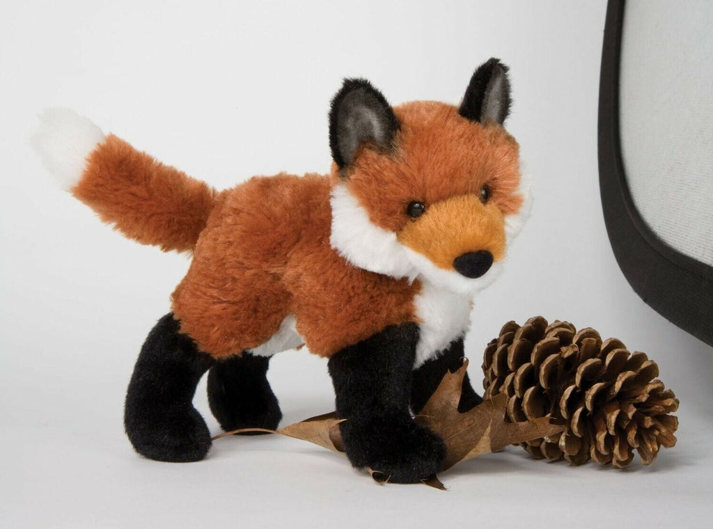Plush red fox standing beside pinecones and autumn leaves